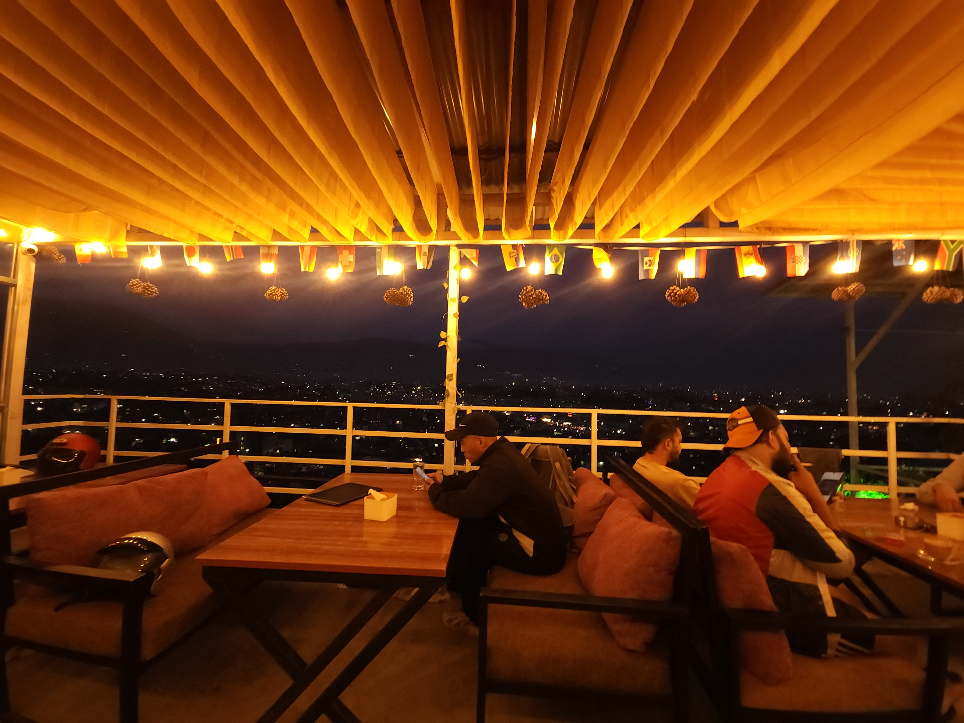 Rooftop terrace at Ask Restro & Bar glowing under a yellow canopy with city lights below at night