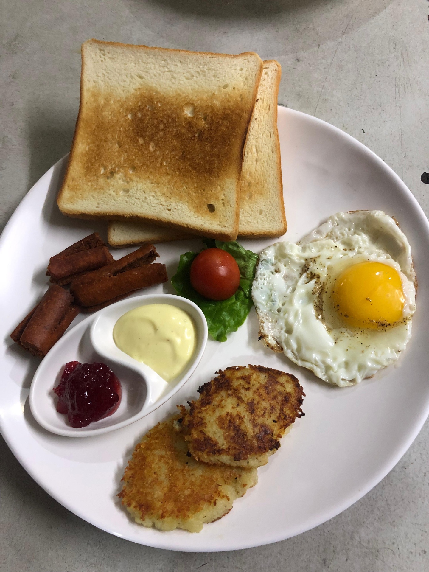Breakfast plate with toast, fried egg, sausages, hash browns, jam and butter