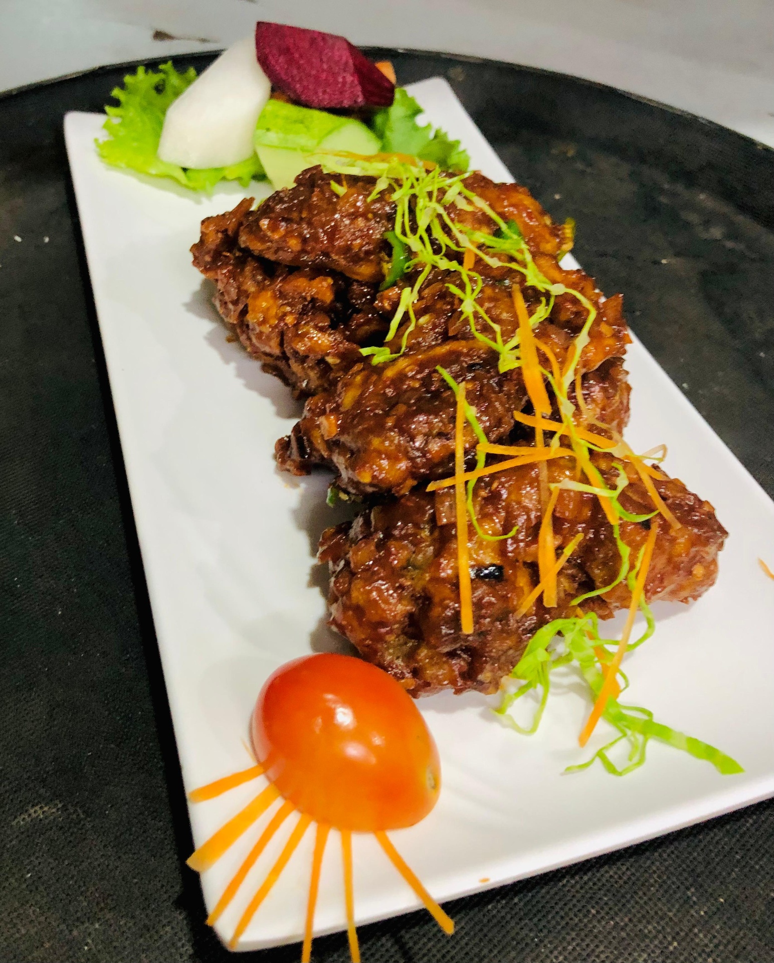 Dark saucy chicken chilli on a rectangular white plate garnished with carrot and cabbage juliennes