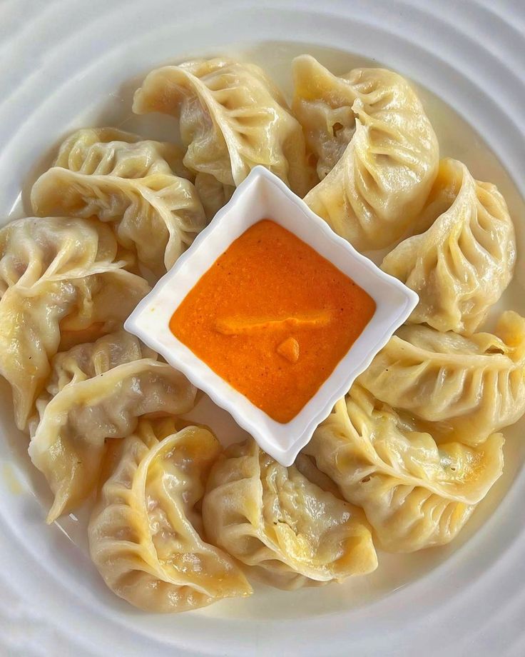 Plate of steamed momo circled around a bowl of tomato achar